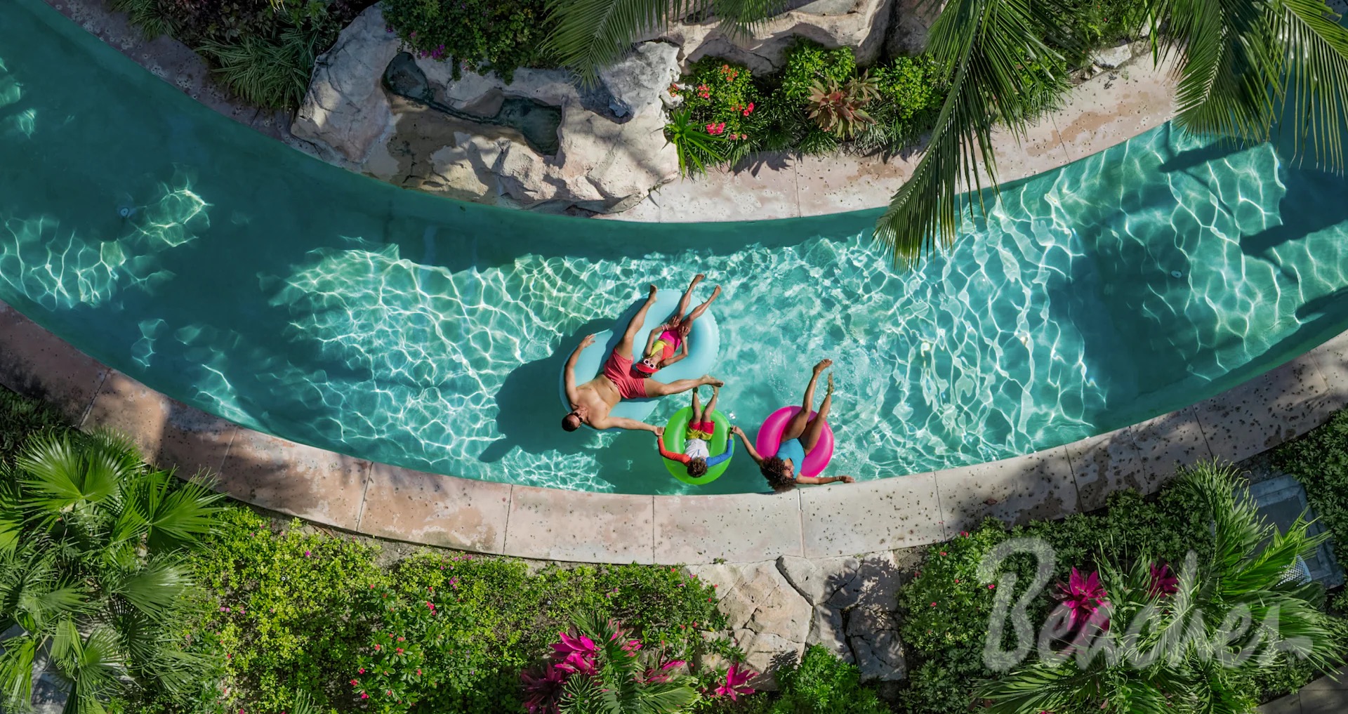 Family floating on tubes in the lazy river surrounded by tropical plants at Beaches Turks & Caicos.