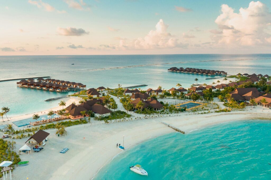 Aerial view of a tropical resort with overwater bungalows and sandy beaches, surrounded by clear blue water and palm trees.
